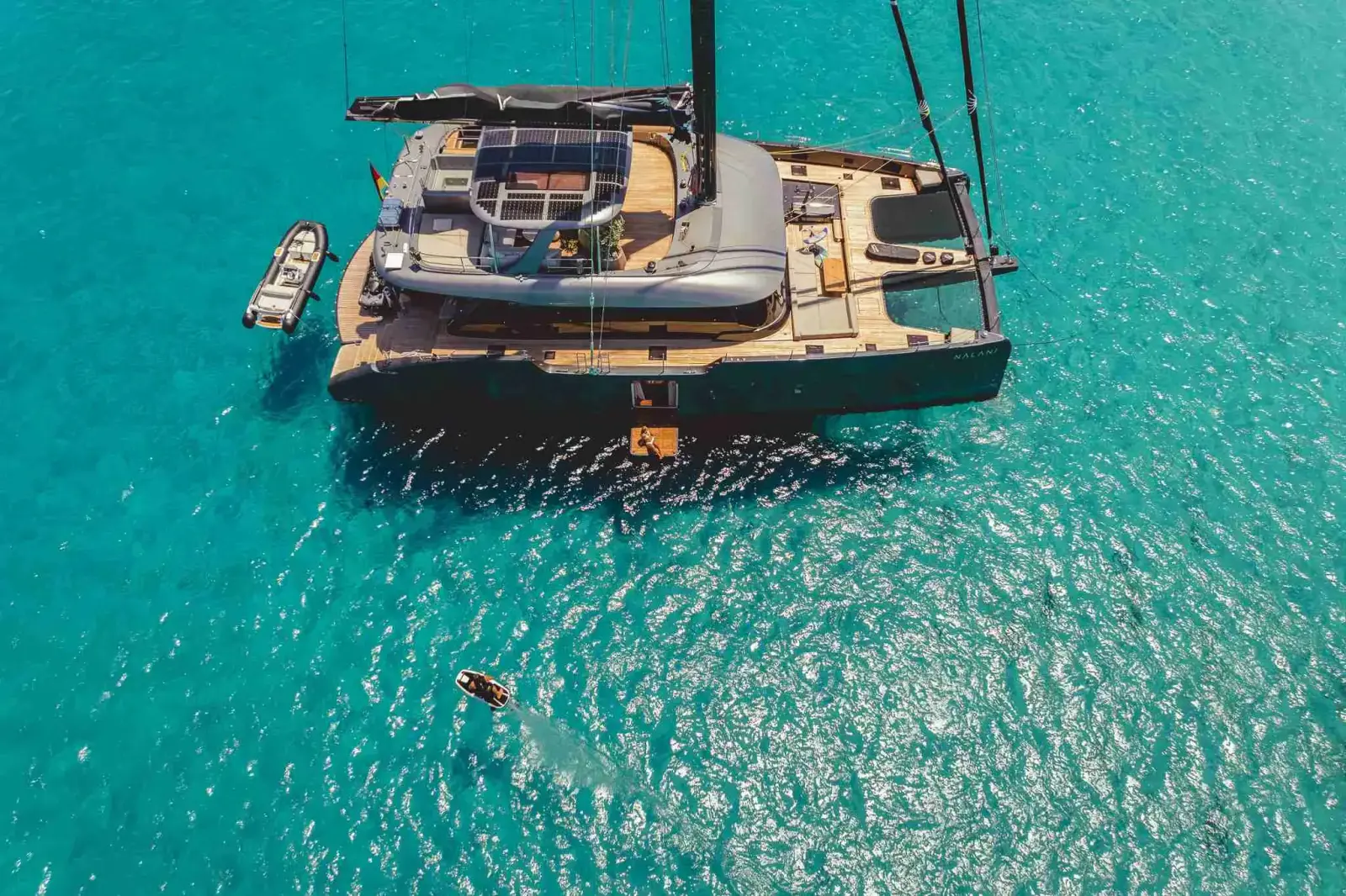 NALANI, a Sunreef 80 Eco sailing catamaran, at anchor over clear turquoise water with her tender alongside